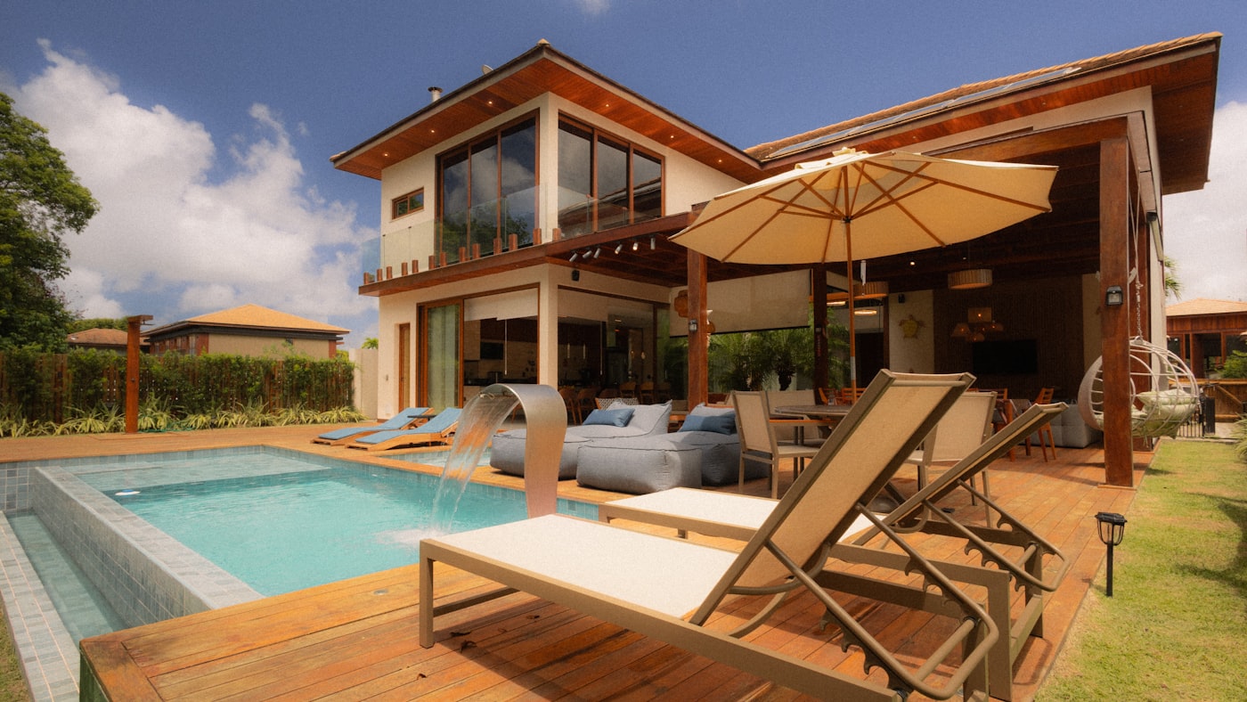 Casa térrea com piscina, deque de madeira e área de estar coberta voltada para o jardim