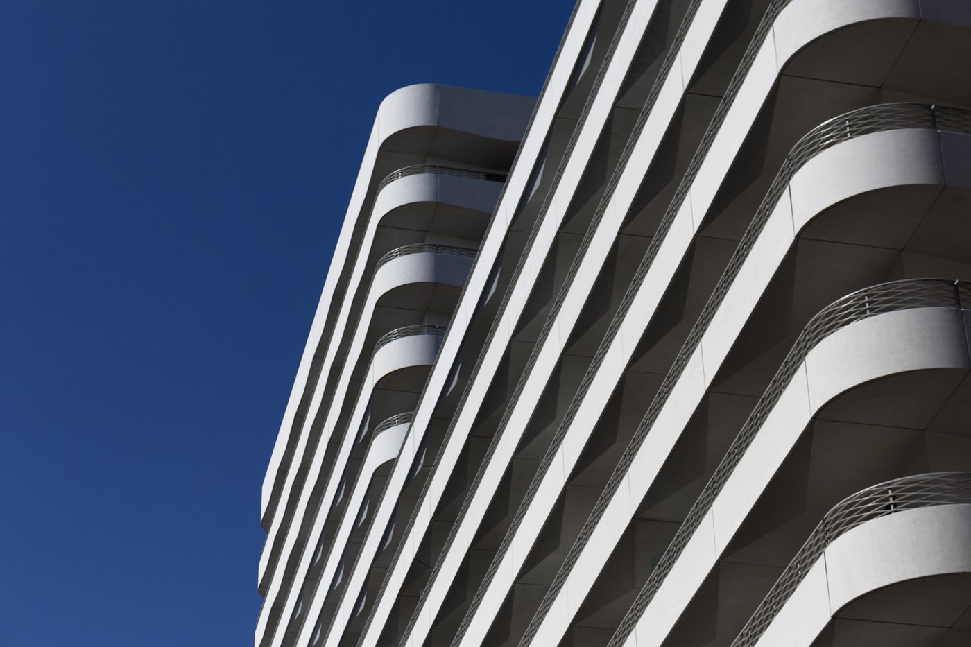 Fachada de edifício em concreto branco vista de baixo, com brises horizontais recortando o céu
