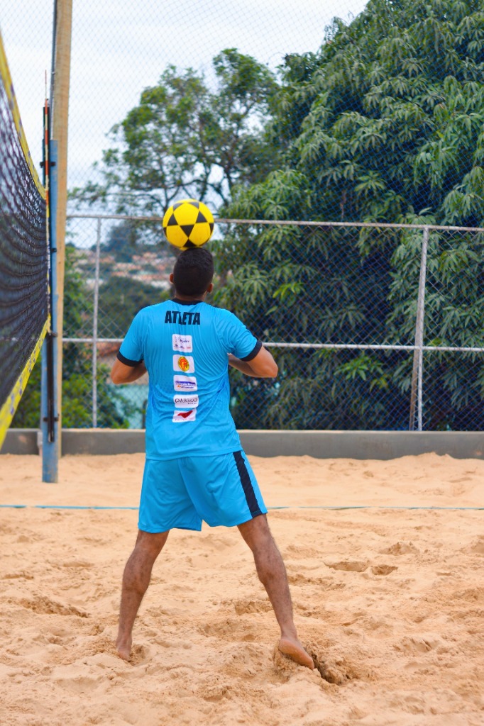 Atleta dominando a bola no peito em quadra de futevôlei